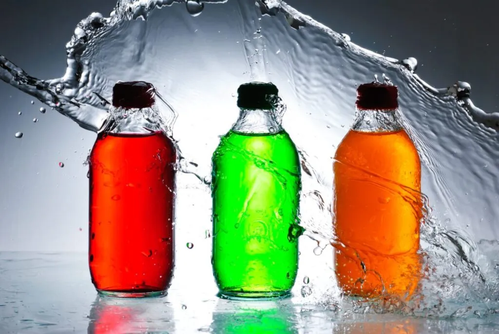 Botellas de plástico con líquidos rojos, verdes y naranjas, representando a las bebidas azucaradas sujetas a discusiones sobre regulación en México.