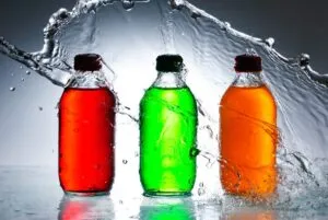 Botellas de plástico con líquidos rojos, verdes y naranjas, representando a las bebidas azucaradas sujetas a discusiones sobre regulación en México.