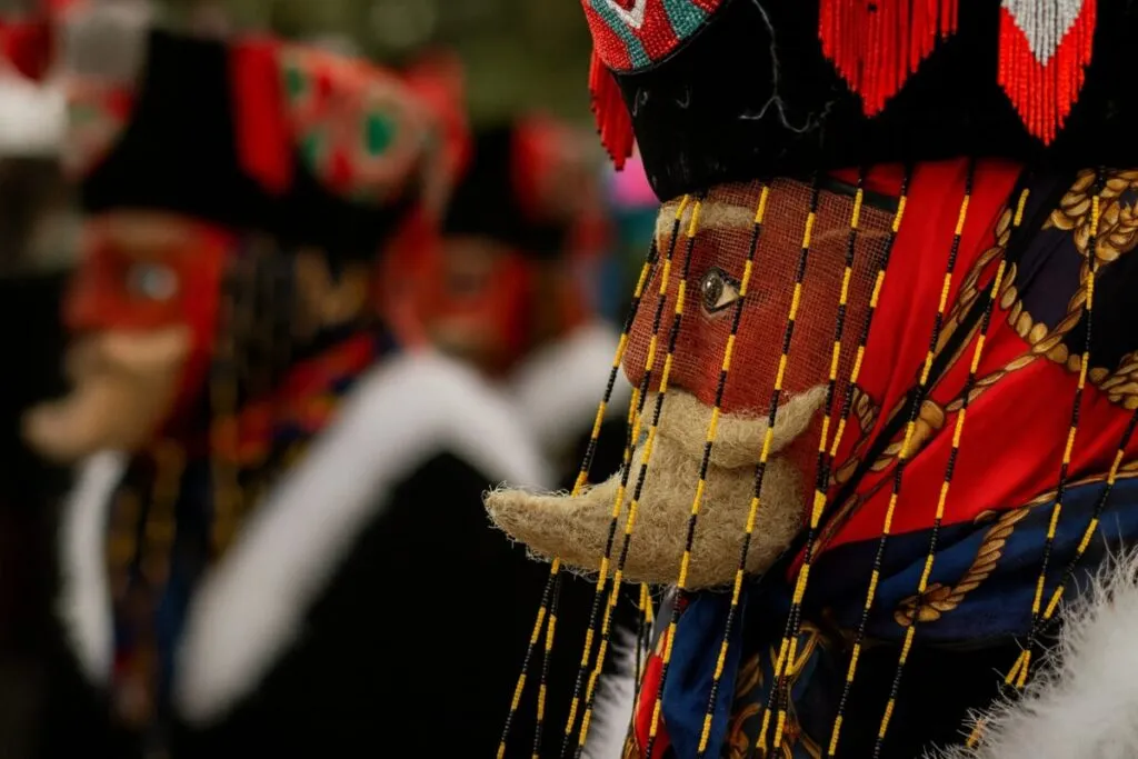 Máscara tradicional de un chinelo de Morelos con colores vibrantes y fondo difuminado de otros danzantes, representando la herencia cultural y artística que inspira la nueva convocatoria para integrar el Consejo de Cultura del estado.