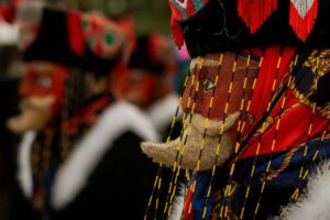 Máscara tradicional de un chinelo de Morelos con colores vibrantes y fondo difuminado de otros danzantes, representando la herencia cultural y artística que inspira la nueva convocatoria para integrar el Consejo de Cultura del estado.