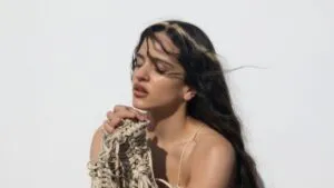 Retrato artístico de Rosalía en un escenario minimalista con estética teatral y luces suaves inspirado en su Lux Tour experimental