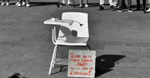 Banca escolar vacía con una rosa blanca y un cartel que dice “Quiero que mi mamá reciba mi título, no mi acta de defunción”, colocada durante una protesta por la violencia contra las mujeres tras el asesinato de la estudiante Kimberly Ramos en Morelos.